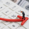 Economic recession, bear stock market or financial crisis concept, miniature businessman standing on red pointing down arrow on white calculator with background of US dollar banknote money.