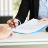 Close up of an executive hands holding a pen and indicating where to sign a contract at office