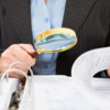 Close-up Of Businessperson Checking Bills With Magnifying Glass